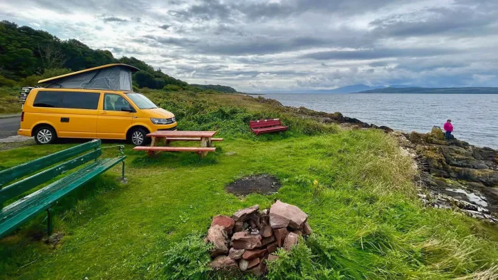 Experience freedom with an RV rental! Bright yellow campervan, picnic setup, fire pit, and person enjoying the rugged coast.. Volkswagen T6 transporter 2019