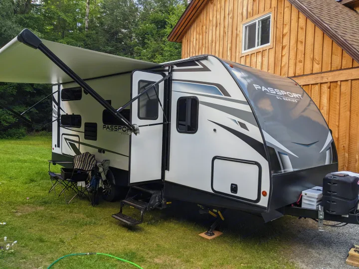 This Passport RV rental, a travel trailer, is parked on grass with its awning extended, ready for an outdoor camping trip.. Keystone RV Passport SL 2021