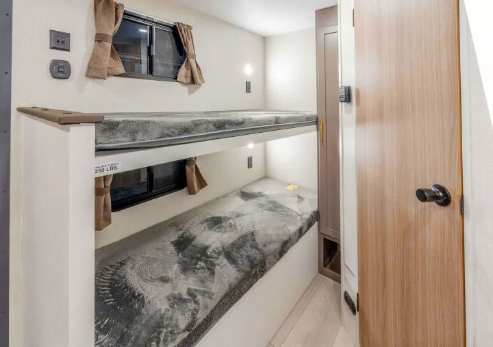 Inside this RV rental, a compact bunk bed room features two cozy beds with windows, curtains, lights, and outlets.. KZ Sportsmen Classic 130BH 2026
