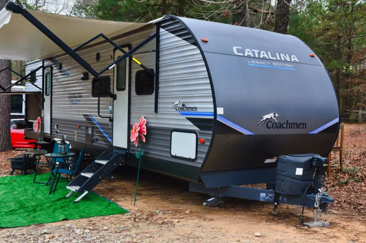 Coachmen Catalina rv rental at a wooded campsite, featuring an awning, outdoor seating, and fire pit.. Coachmen Catalina 2022
