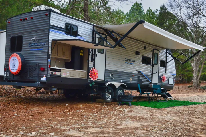 This Coachmen Catalina travel trailer, available for rv rental, features an open outdoor kitchen, extended awning, and a cozy camping setup.. Coachmen Catalina 2022