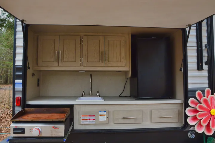 This rv rental's outdoor kitchen features a sink, griddle, fridge, and cabinets, ideal for camping and outdoor cooking.. Coachmen Catalina 2022