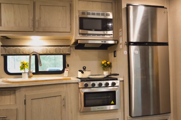 Sleek RV rental kitchen: stainless steel microwave, oven, fridge, light wood cabinets, sink, and a view of nature.. Coachmen Catalina 2022