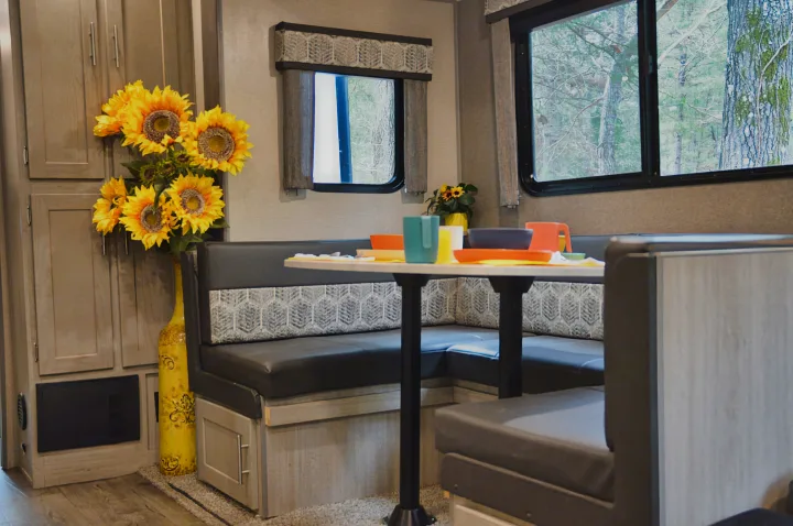 This inviting RV rental interior features a U-shaped dinette, colorful tableware, and cheerful sunflowers by the window.. Coachmen Catalina 2022