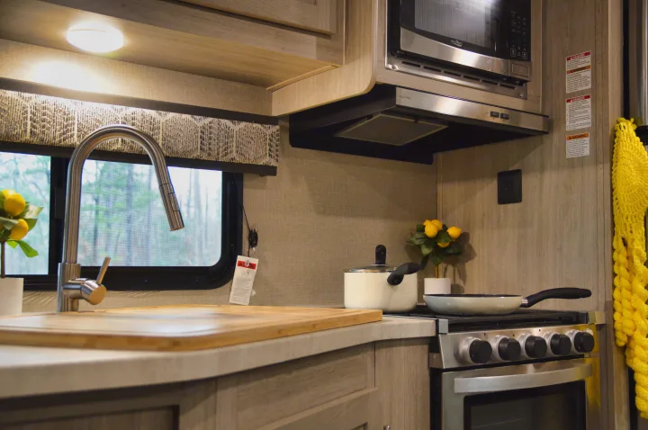 This RV rental kitchen offers a compact space with a sink, stove, microwave, and cookware for convenient road trip cooking.. Coachmen Catalina 2022