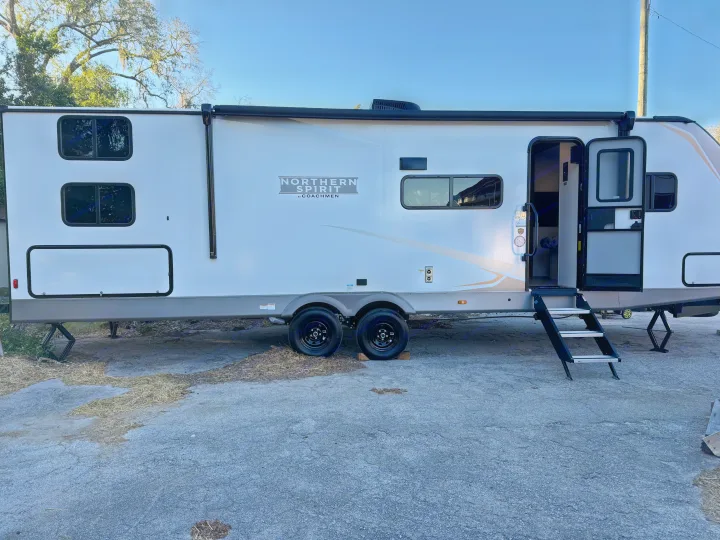 White Northern Spirit travel trailer RV rental, parked outdoors with steps down and door open, awaiting its next adventure.. Coachmen Spirit 29BH 2026