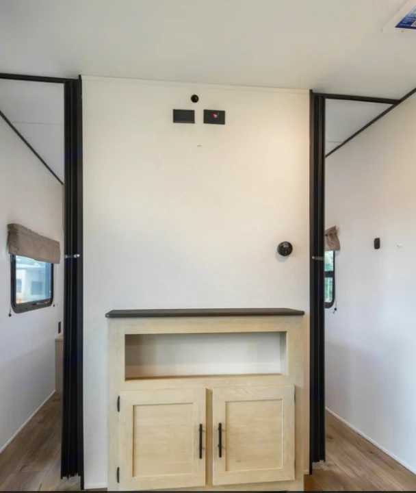 Inside this RV rental: A modern entertainment wall with light wood cabinetry, TV hookups, and thermostat, leading to open living areas.. Forest River Shasta I-5 2025