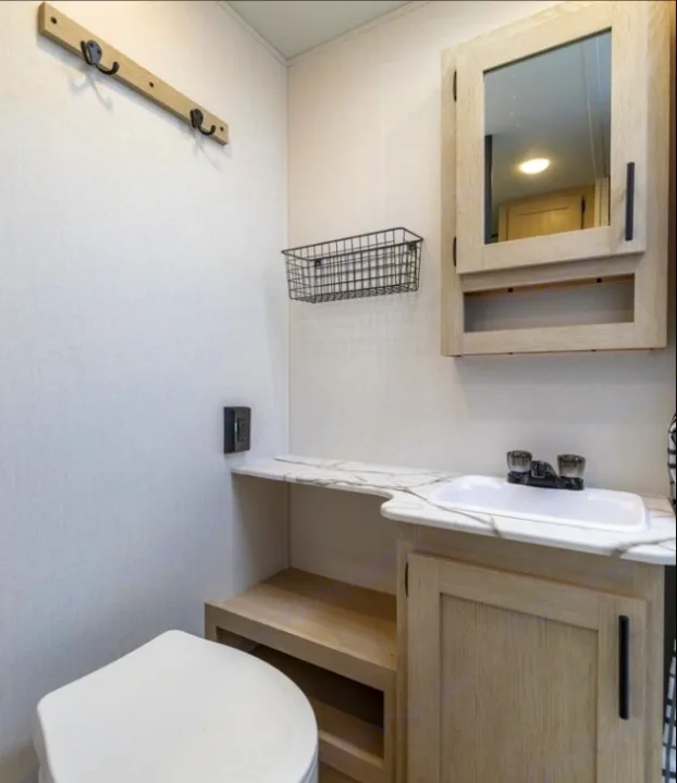 Clean RV rental bathroom featuring a toilet, sink, mirrored cabinet, wall basket, and hooks for storage.. Forest River Shasta I-5 2025