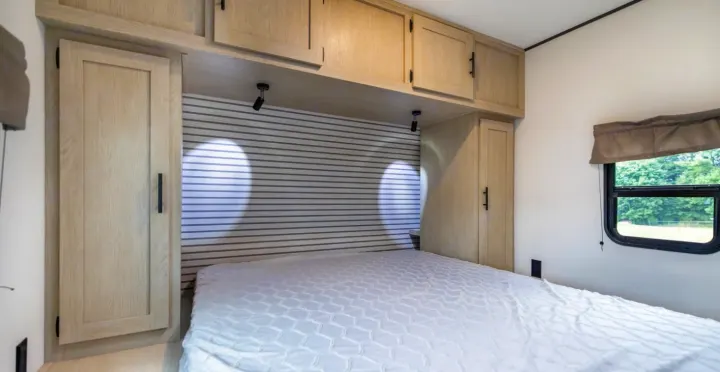 Comfortable RV rental bedroom with a white bed, overhead cabinets, bedside wardrobes, and a window for scenic views.. Forest River Shasta I-5 2025