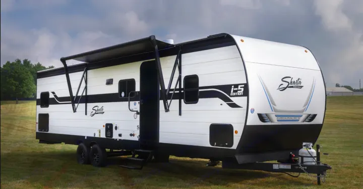 This white Shasta travel trailer, with an extended awning, is parked on grass. Ideal for an outdoor RV rental adventure.. Forest River Shasta I-5 2025