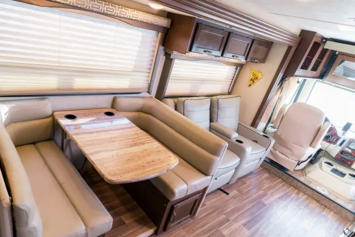 Spacious RV rental interior featuring a light-colored dinette, theater seats, and driver's cockpit with wood accents.. Thor A.C.E. 2018