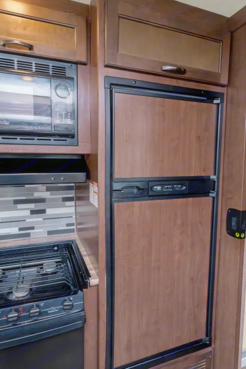 Modern RV rental kitchen with a microwave, gas stovetop, and wood-paneled fridge, featuring a stylish backsplash.. Thor A.C.E. 2018