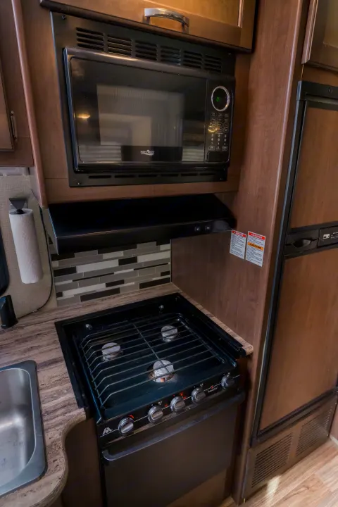 RV rental kitchen: High Pointe microwave, 3-burner Wedgewood Vision stove/oven, sink, fridge, and tiled backsplash.. Thor A.C.E. 2018