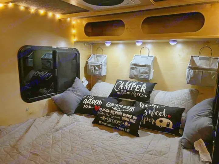Inviting RV rental interior: a comfy bed with "Camper Our Happy Place" pillows, ambient lights, and a window for camping adventures.. Outbound Trailer Outbound Extreme 2026