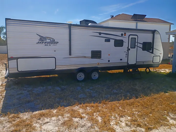 White Jayco Jay Flight SLX travel trailer for rv rental, parked on dry grass in the sun. Ideal for outdoor adventures.. Jayco Jay Flight SLX 2017