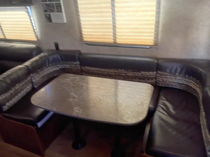 RV rental dinette featuring dark upholstered U-shaped seating, a light table, and windows with horizontal blinds.. Jayco Jay Flight SLX 2017