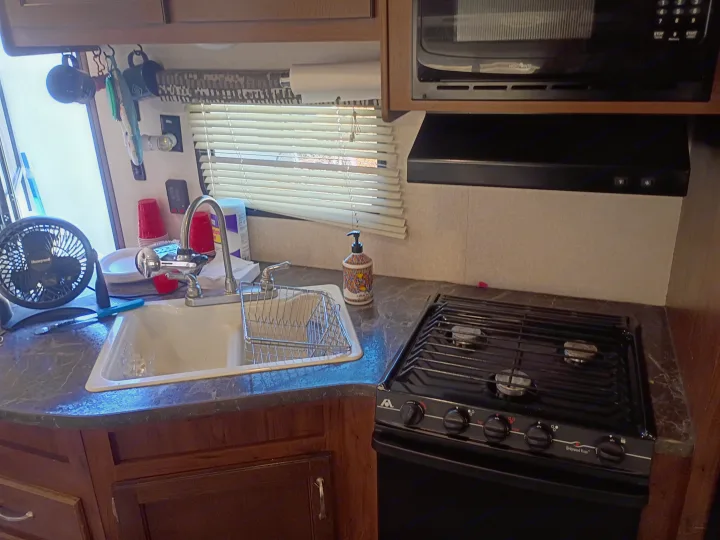 Compact rv rental kitchen: sink, gas stove, microwave, and a small fan near the window.. Jayco Jay Flight SLX 2017