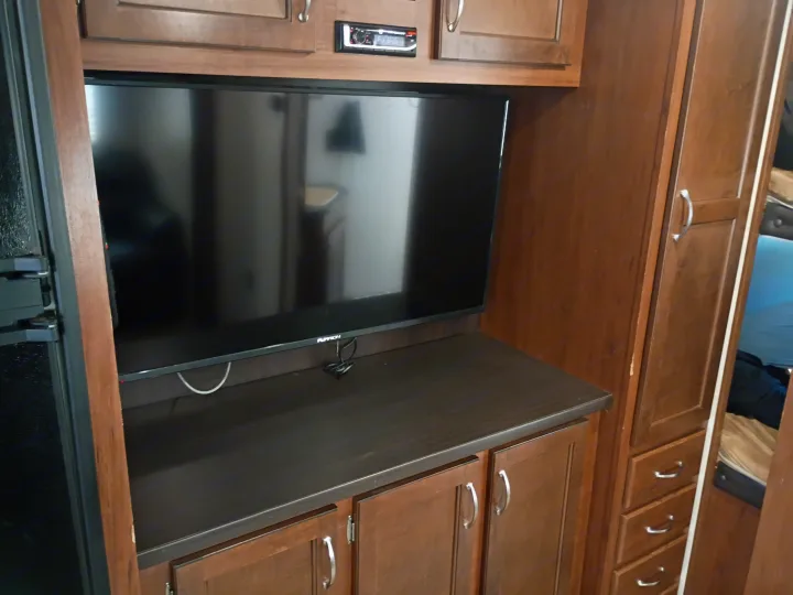 RV rental living area with a mounted TV, built-in stereo, refrigerator, and dark wood cabinetry.. Jayco Jay Flight SLX 2017