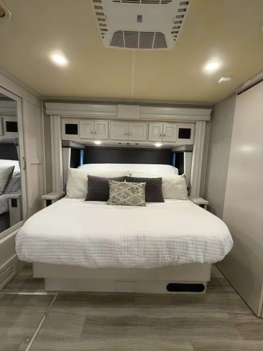 Modern RV rental bedroom with a cozy bed, overhead storage, and a ceiling AC unit, offering comfort for your journey.. Holiday Rambler Nautica 2021