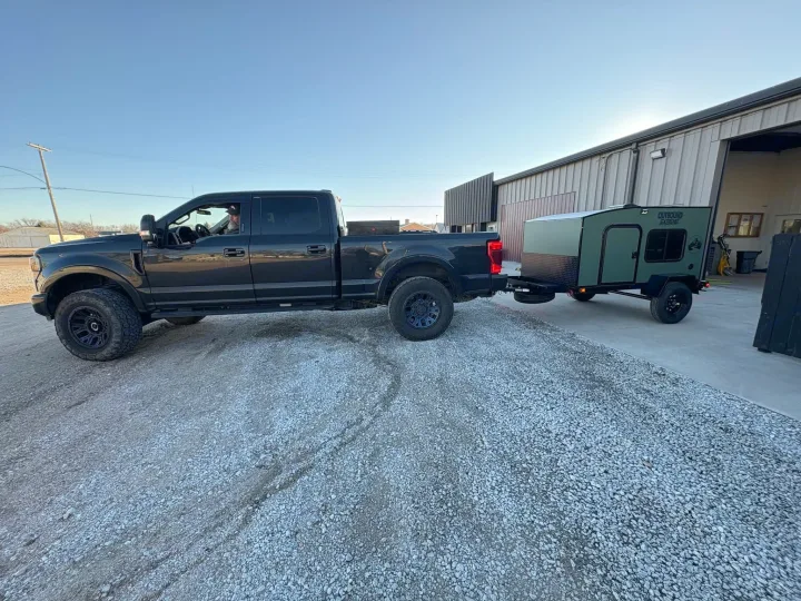 A dark truck tows an Outbound Extreme camper on gravel, ready for your RV rental adventure.. Outbound Trailer Outbound Extreme 2026
