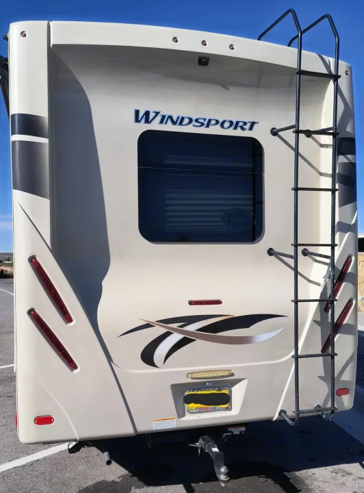 Cream-colored Windsport RV rental, showing the rear with a ladder, window, and hitch receiver. Perfect for your next road trip.. Thor Windsport 2017