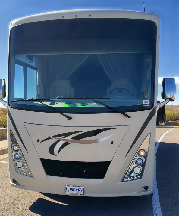 A cream-colored Class A RV rental, seen from the front, showcasing its large windshield, sleek design, and distinct headlights.. Thor Windsport 2017