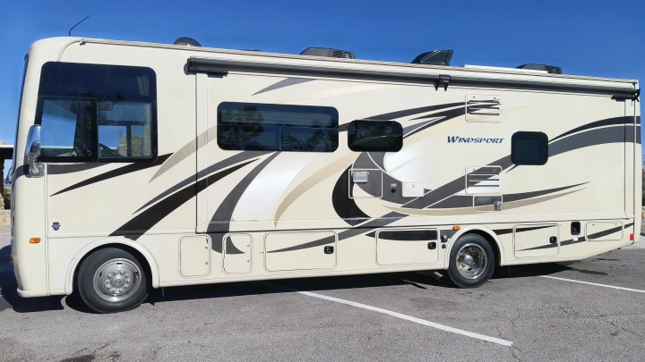 This cream-colored RV rental with striking graphics is ready for adventure. Parked on asphalt under a clear sky.. Thor Windsport 2017