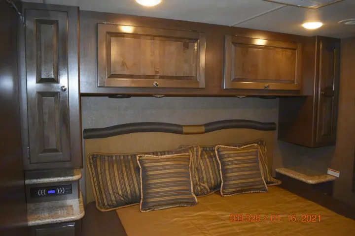 Cozy RV rental bedroom with warm wooden cabinets, plush headboard, and striped pillows, offering comfort and ample storage.. Thor Windsport 2017