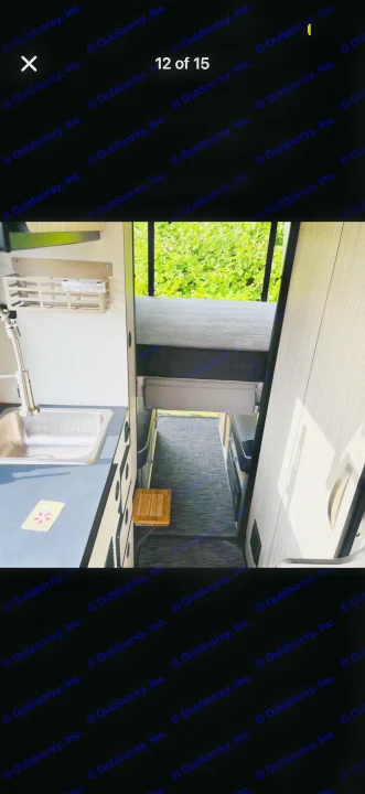 RV rental interior showing a compact kitchen with sink, storage, and a thermometer, plus an upper bed and narrow walkway.. Winnebago Revel 2022