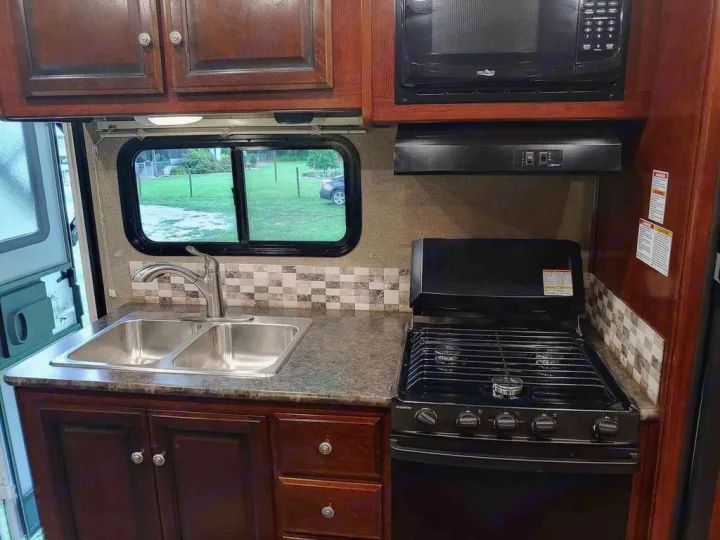 Fully equipped rv rental kitchen featuring a double sink, microwave, gas stovetop, and dark wood cabinets. Perfect for camping!. Holiday Rambler Altera 2018