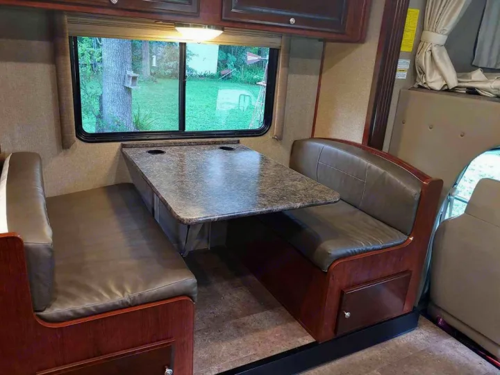 This RV rental features a cozy dinette with booth seating, a table with cupholders, and a scenic window view.. Holiday Rambler Altera 2018