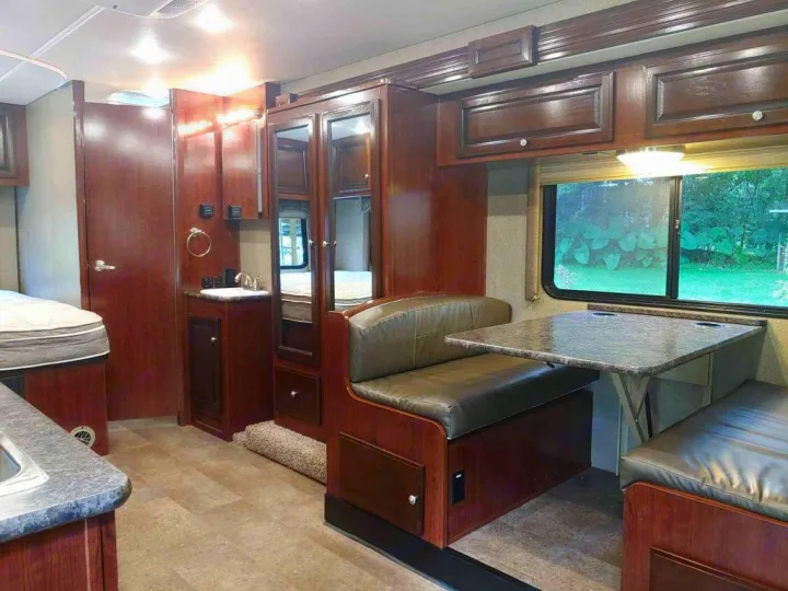 Explore this RV rental's interior: a dinette, vanity with sink, bed, and dark wood cabinetry on light floors.. Holiday Rambler Altera 2018