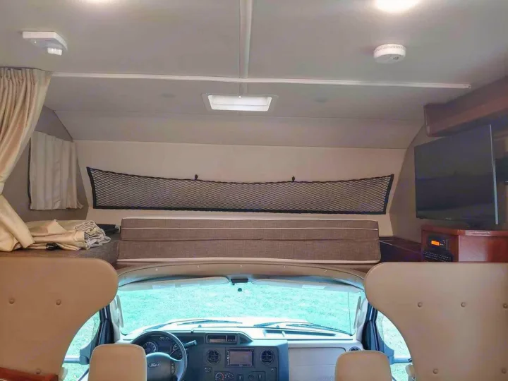**RV rental** interior: Front view showing cab-over bunk with safety net, cockpit, TV, and ceiling safety detector.. Holiday Rambler Altera 2018