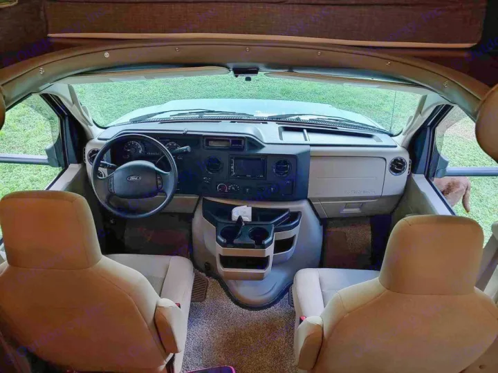 Spacious RV rental cockpit with Ford dashboard, driver/passenger seats, and a brown dog visible outside.. Holiday Rambler Altera 2018