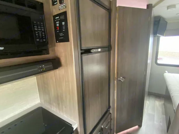 Explore this RV rental's kitchen, featuring a microwave, two-door fridge, stovetop, and nearby interior door.. Winnebago Spirit R24742 2025