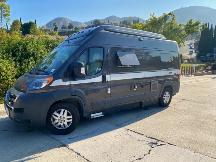 Dark gray camper van, ideal for your next rv rental adventure, parked on a sunny street with scenic hills behind it.. Hymer Hymer Class B 2019