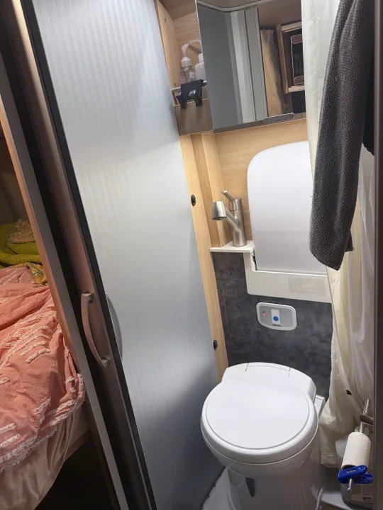 Compact RV rental bathroom featuring toilet, small sink, mirror, shower curtain, and toiletries, maximizing travel space.. Hymer Hymer Class B 2019
