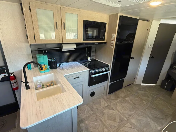 Modern rv rental kitchen with light wood cabinets, black appliances, and a full sink for travelers.. Forest River Salem Cruise Lite Platinum 2023