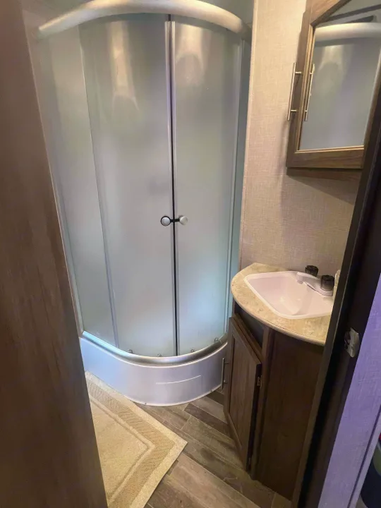 RV rental bathroom features a frosted glass curved shower and corner sink with vanity, ideal for compact travel.. Crossroads RV Zinger 2024