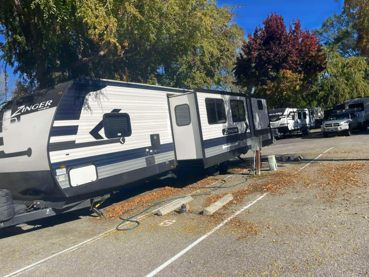 A modern Zinger travel trailer rv rental with slide-outs extended, parked in a sunny autumn campground with fall leaves.. Crossroads RV Zinger 2024