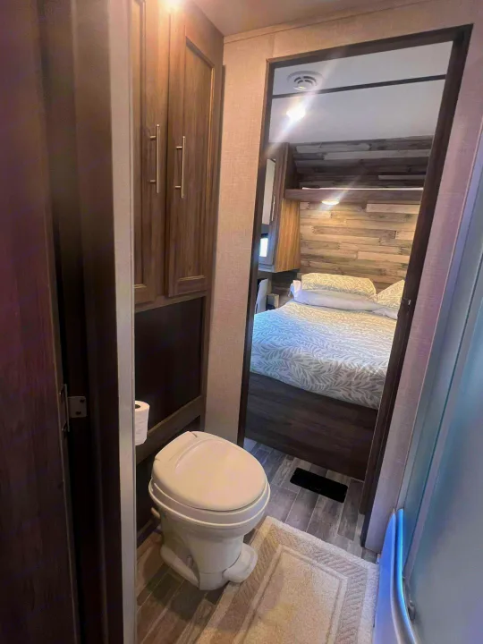 Compact RV rental interior: A small bathroom with toilet, offering a clear view into the adjacent cozy bedroom for travel.. Crossroads RV Zinger 2024