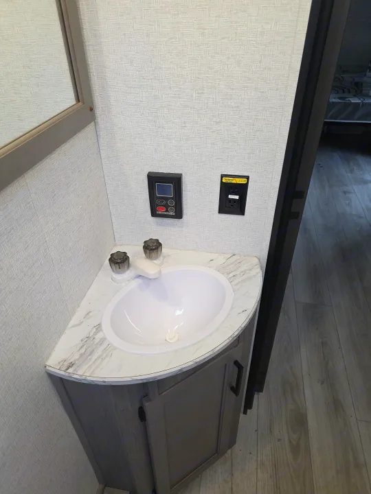 RV rental bathroom interior: a small vanity with white sink, water heater controls, and solar-powered outlet on the wall.. Keystone RV Hideout 2025