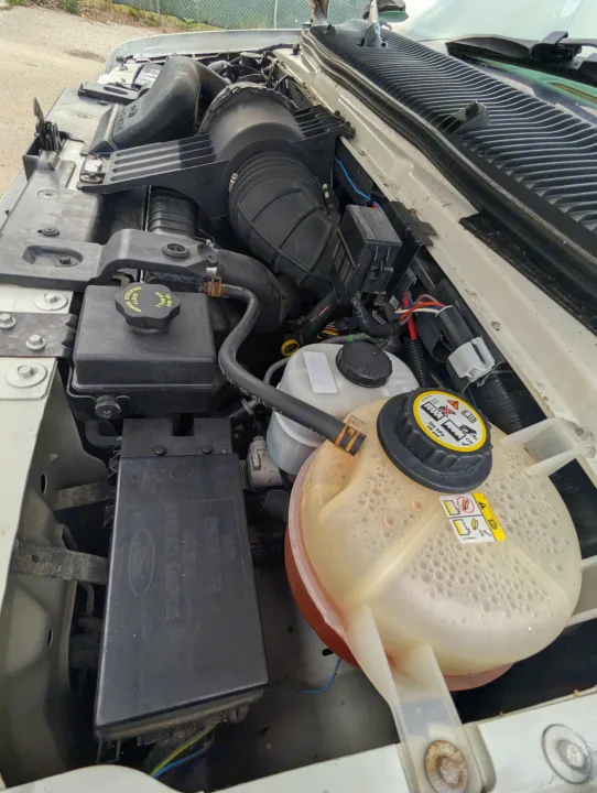 RV rental's open hood shows the engine bay with power steering reservoir, fuse box, and coolant tank with bubbles.. Triple E Regency 2006