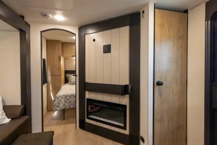 Inviting RV rental interior showcasing a cozy bedroom, electric fireplace, and a light wood door, offering comfort for travel.. Forest River Cherokee Grey Wolf 2025