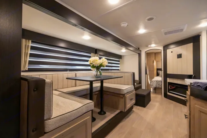 Inside this modern RV rental, a well-lit dinette with comfortable bench seating and a table is visible, offering a cozy dining space.. Forest River Cherokee Grey Wolf 2025