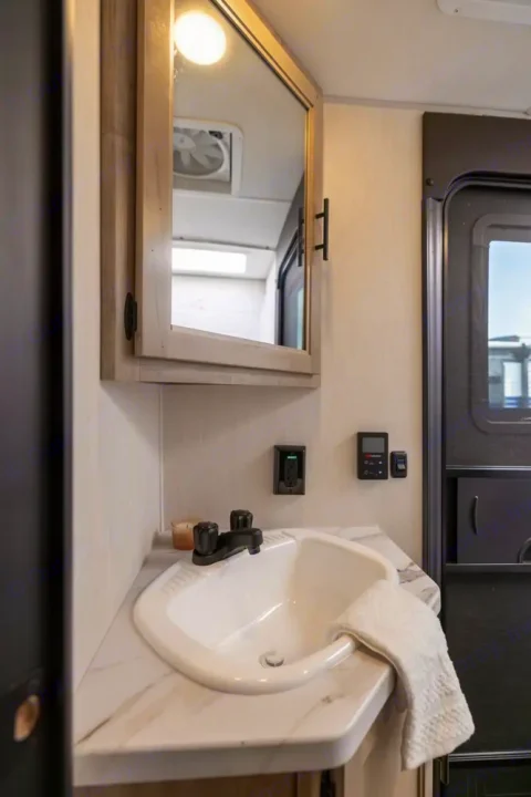 This RV rental features a clean and functional bathroom with a vanity, sink, mirror, and accessible wall controls, ready for your trip.. Forest River Cherokee Grey Wolf 2025