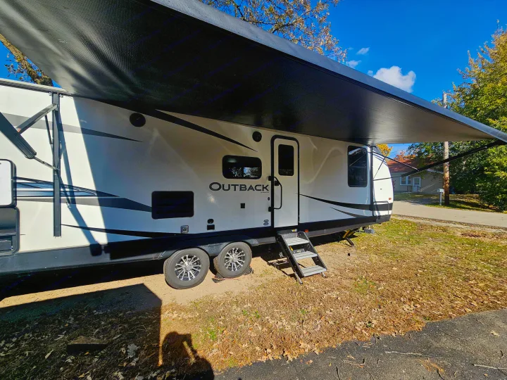 This Outback **rv rental** features a large awning & easy-access steps, parked on a sunny day. Your next outdoor adventure awaits!. Keystone RV Outback Ultra-Lite 2021