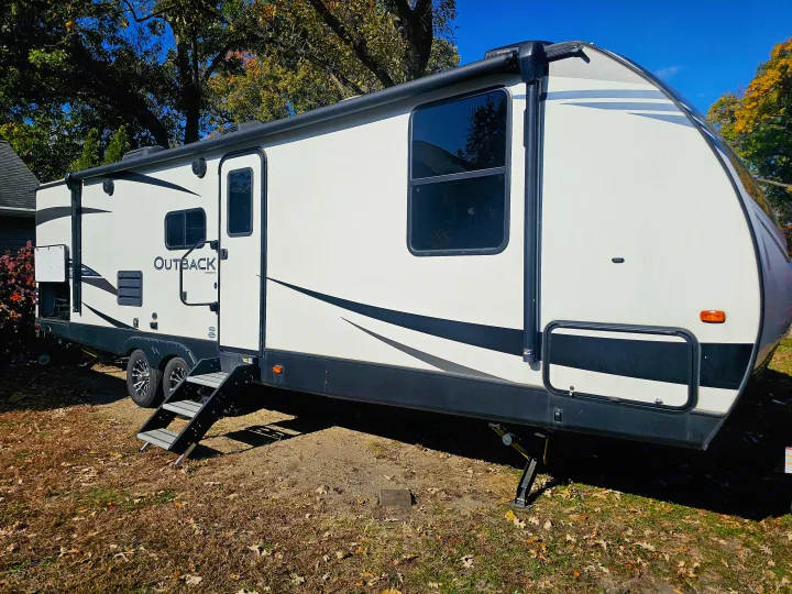This white & black Outback RV rental is a travel trailer parked on dried grass under a sunny blue sky.. Keystone RV Outback Ultra-Lite 2021