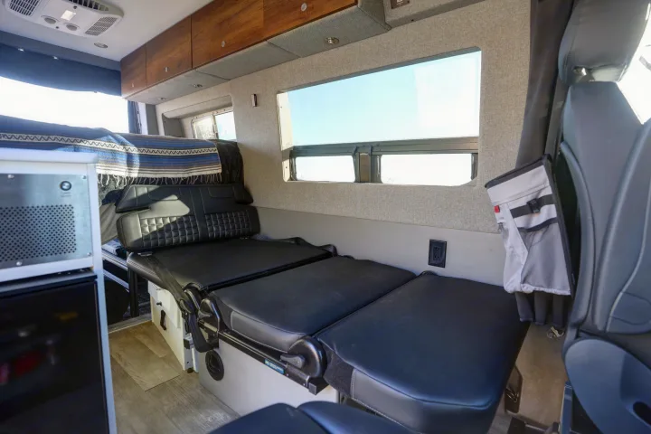 RV rental's versatile interior featuring convertible black leather seating/bed, wood overhead cabinets, and large windows.. Mercedes-Benz Sprinter 2021