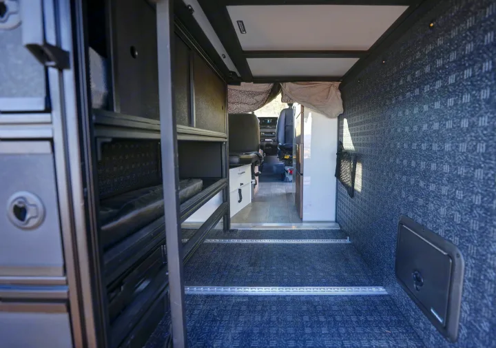 Spacious RV rental interior featuring modular storage, textured walls & floor with cargo rails, and a clear view to the cab.. Mercedes-Benz Sprinter 2021